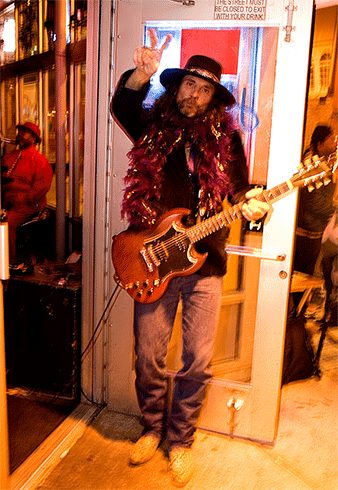 picture of guitarist standing at club door making peace sign