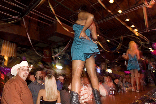 man looks at camera as girl dances on bar