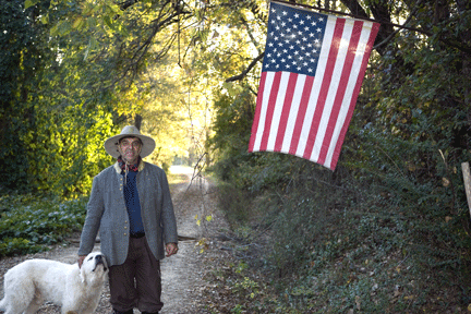 Picture of man and dog standing in country road with flag posted above